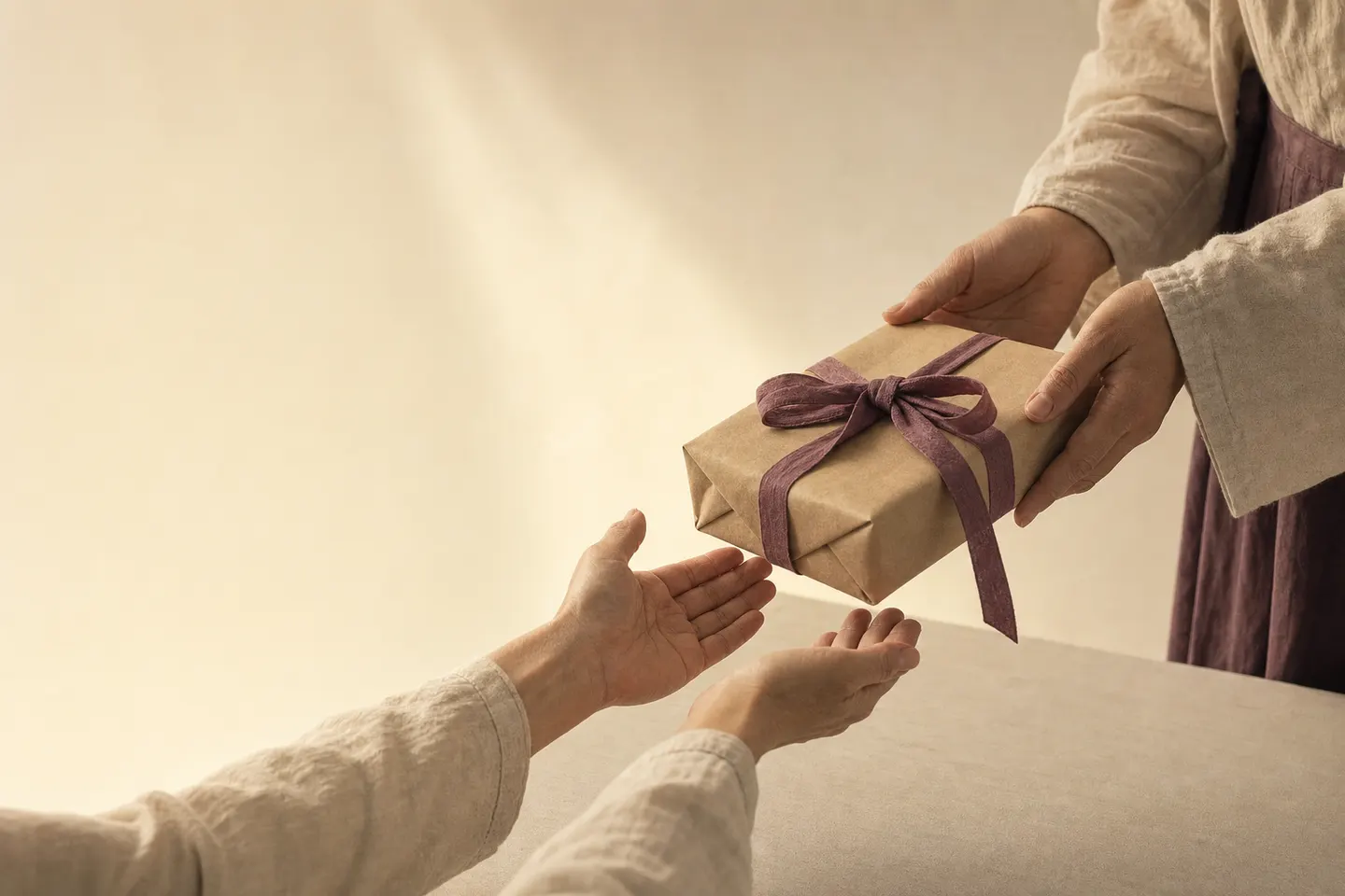 Hands passing a wrapped care package tied with plum ribbon into receiving hands