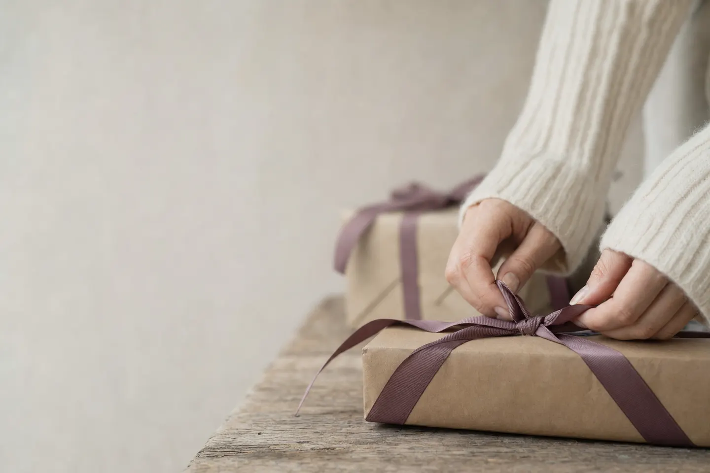 Hands tying a plum ribbon around a wrapped parcel