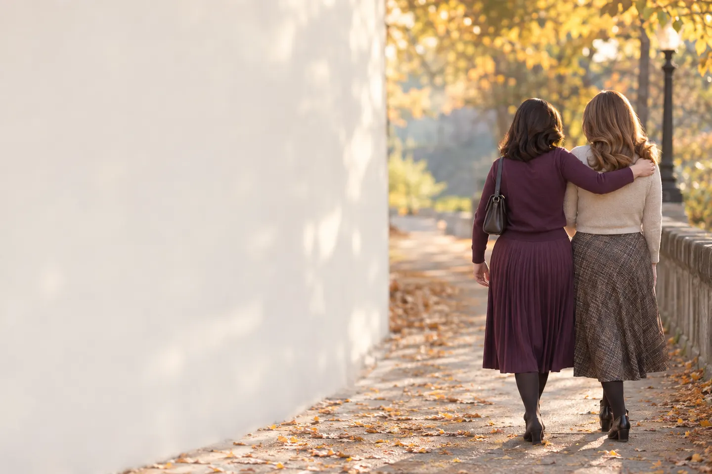 Two women walking together along an autumn path, one with her arm around the other